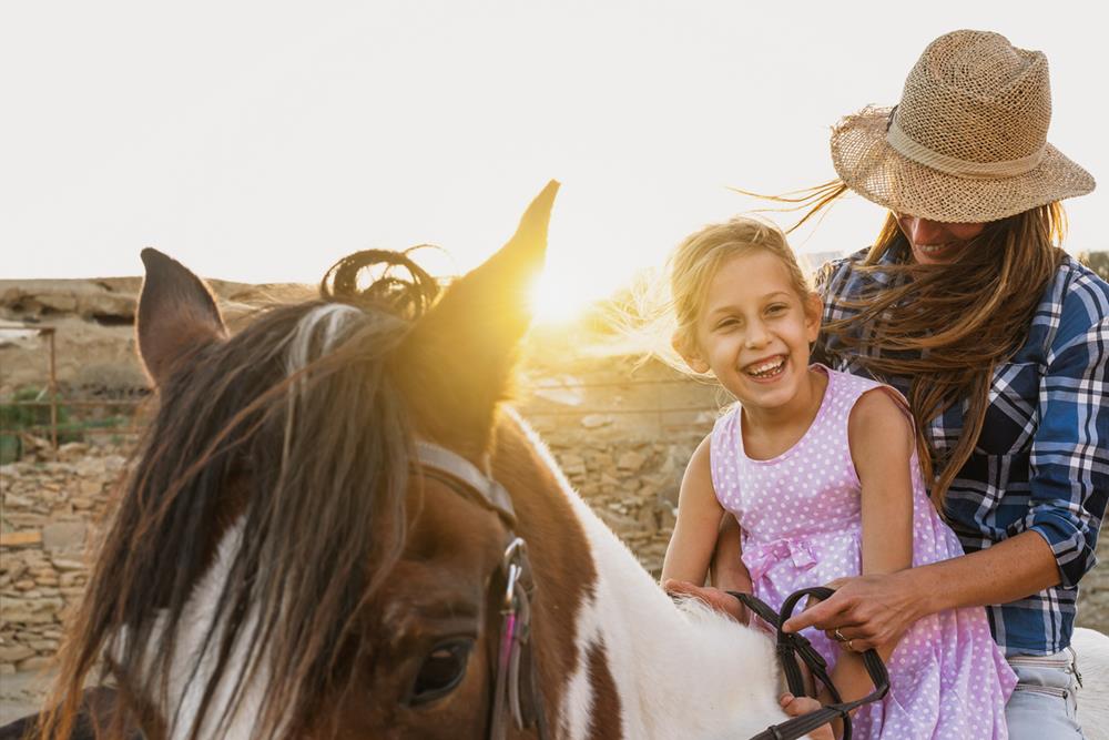 Happy family mother and daughter having fun riding horse inside ranch