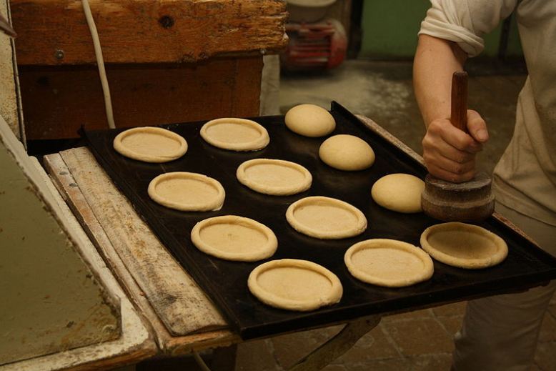 a hand holding a bread presser, pressing a dough forming circle-shaped bread, Kolach