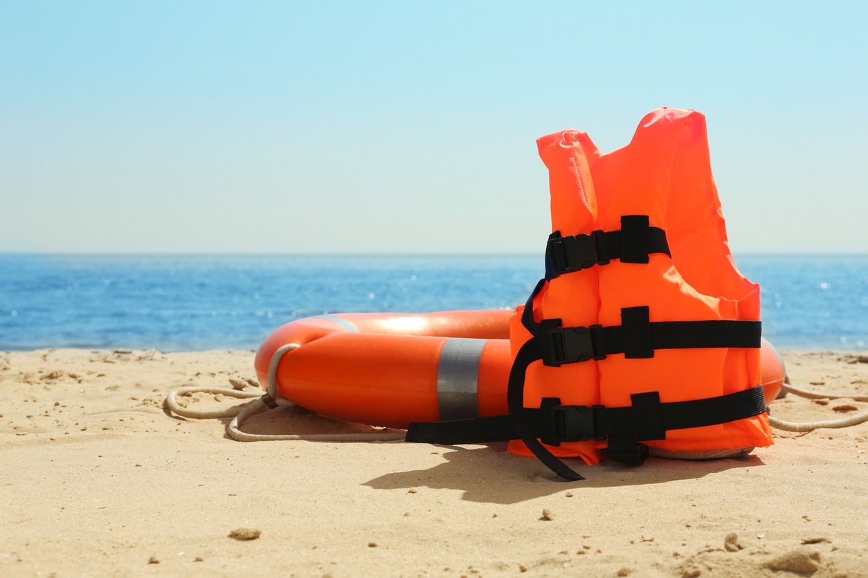 Orange life jacket and buoy on sandy beach near sea