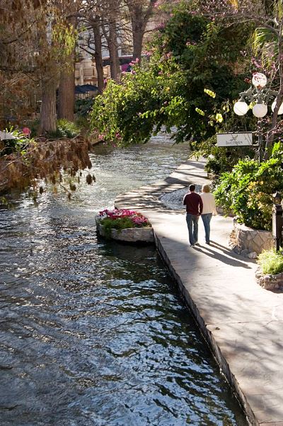 a couple strolling along the Riverwalk by Las Canarias restaurant