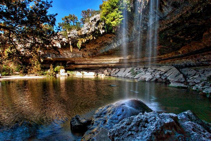 a waterfall flowing freely into Hamilton Pool, which is surrounded by a collapsed grotto