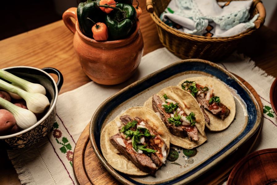 tacos on a ceramic plate, a pot of vegetables, a basket, a jug of vegetables