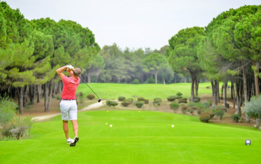 a man wearing a red top playing golf at a golf course