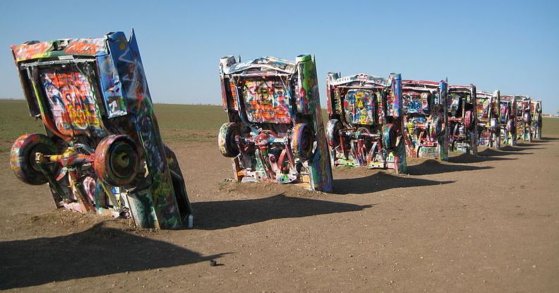 a row of brightly painted Cadillacs half buried in the sand