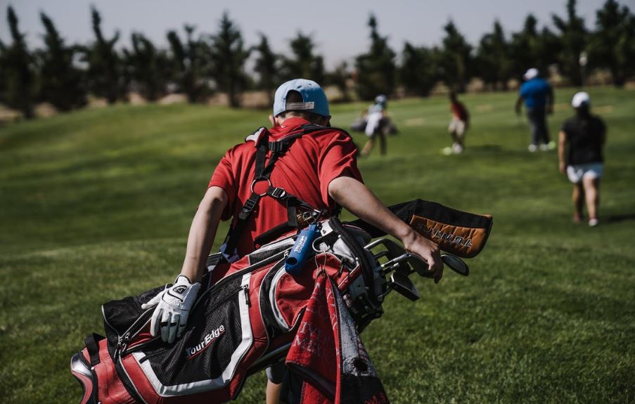 A man walking on the golf field while carrying a black and red golf bag