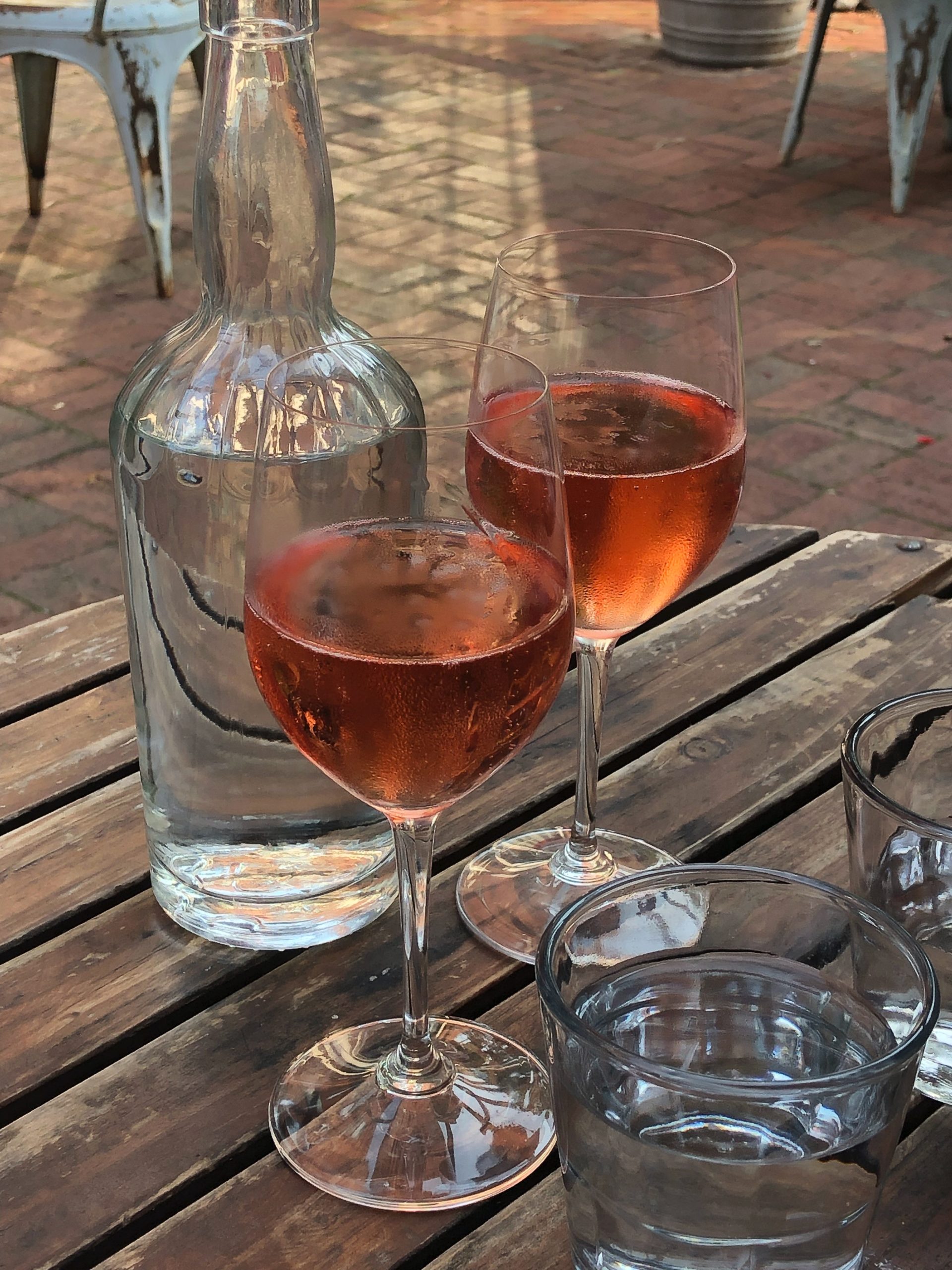 rose wine on wine glasses, and glasses of water on a wooden table outdoor