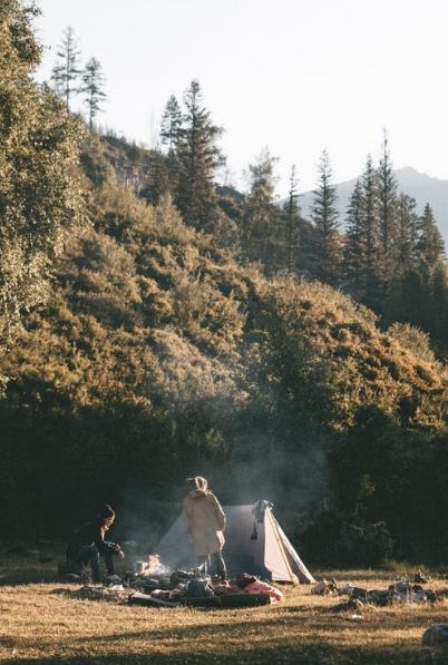 travelers in camping attire, and a tent in a forest