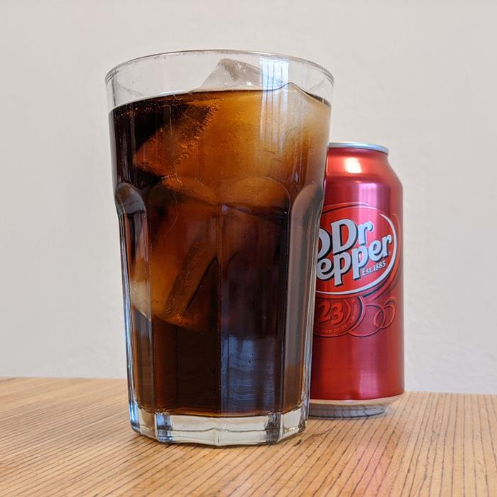 A Dr Pepper drink with ice on a glass, with a can on the back