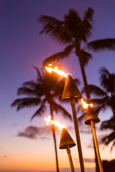 Hawaii sunset with lit tiki torches. Hawaiian icon, lights burning at dusk at beach resort or restaurants for outdoor lighting and decoration, cozy atmosphere.