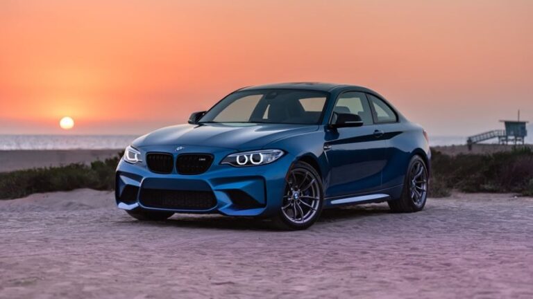 a BMW on a white sand beach during sunset
