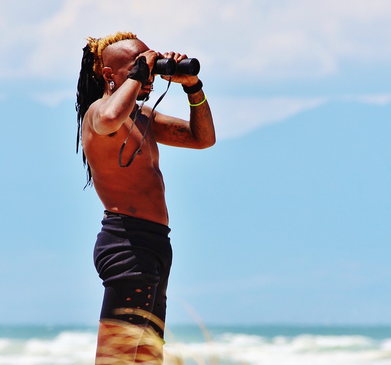 a man using binoculars, seawater, blue sky, grass