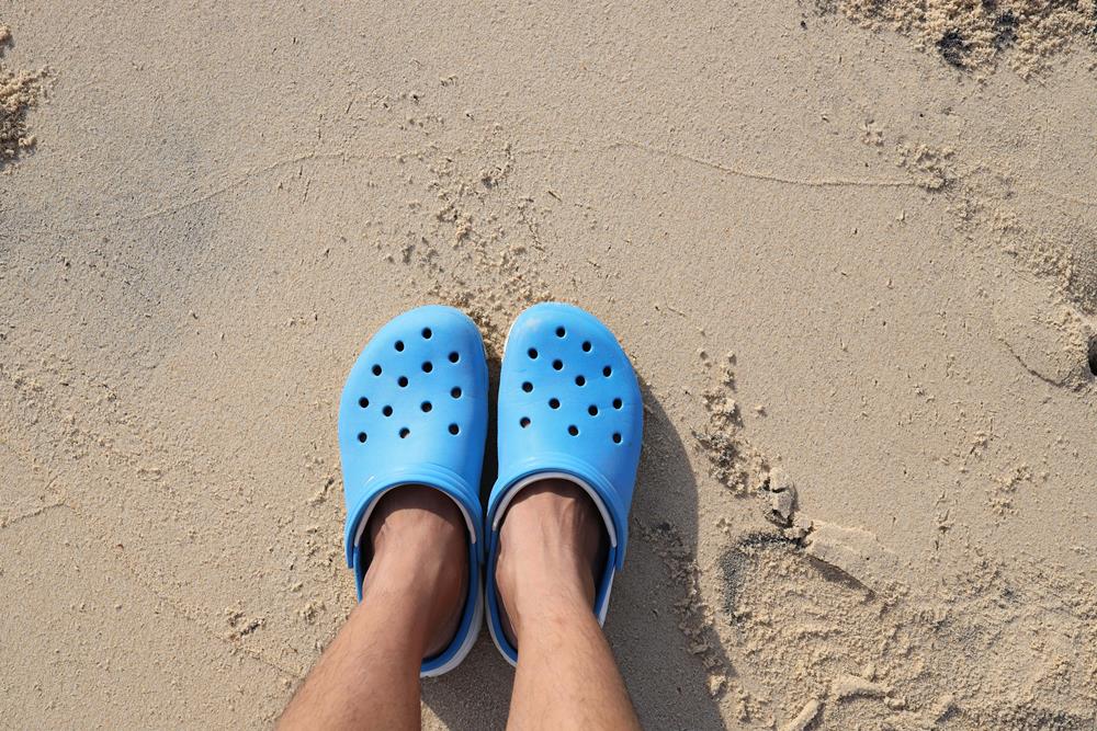 A person wearing blue rubber clogs standing on sand