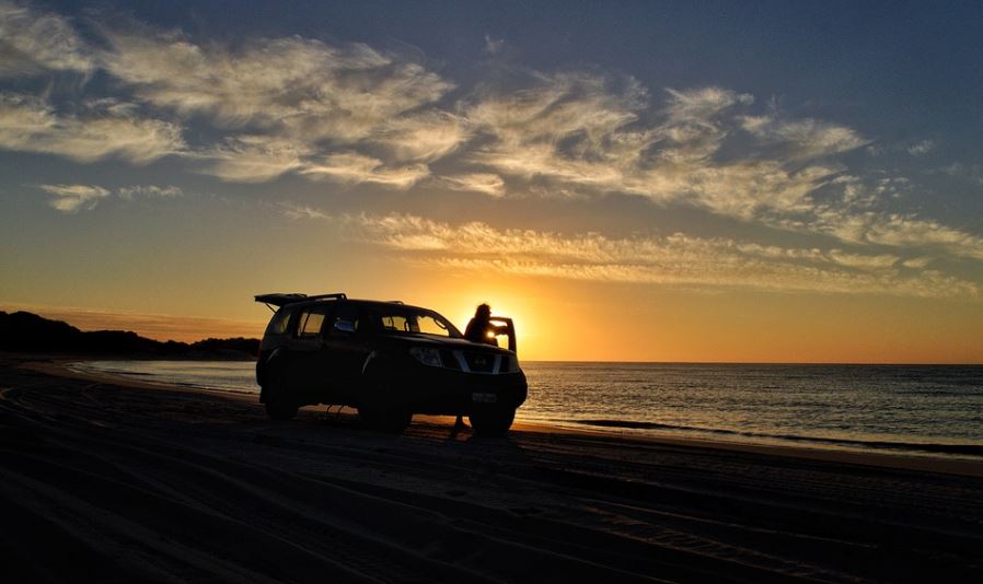 silhouette of a man getting out of his car on a beach during sunset