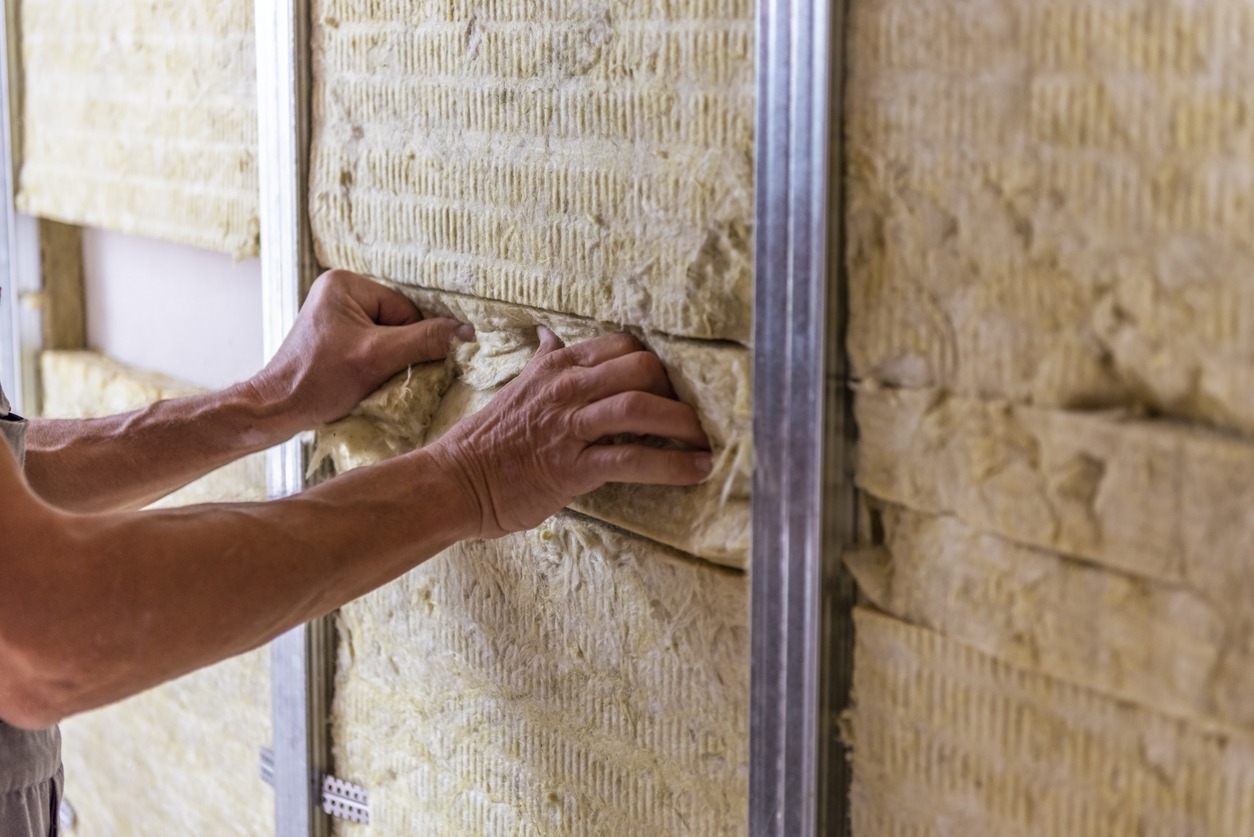 Worker insulating a room wall with mineral rock wool thermal insulation