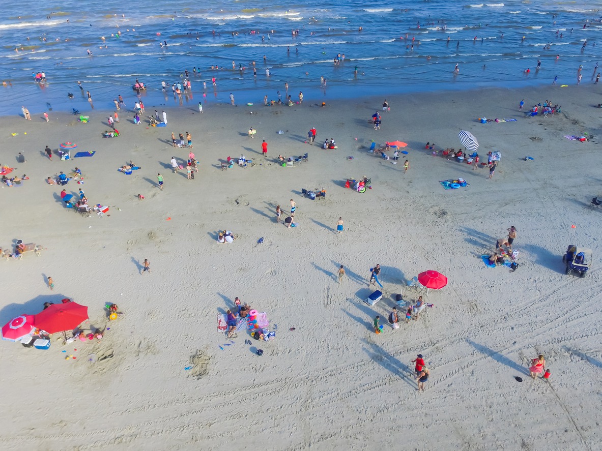 Aerial view beach shoreline on sunny summer day with people bathing, sunbathing, and relaxing in Galveston, Texas