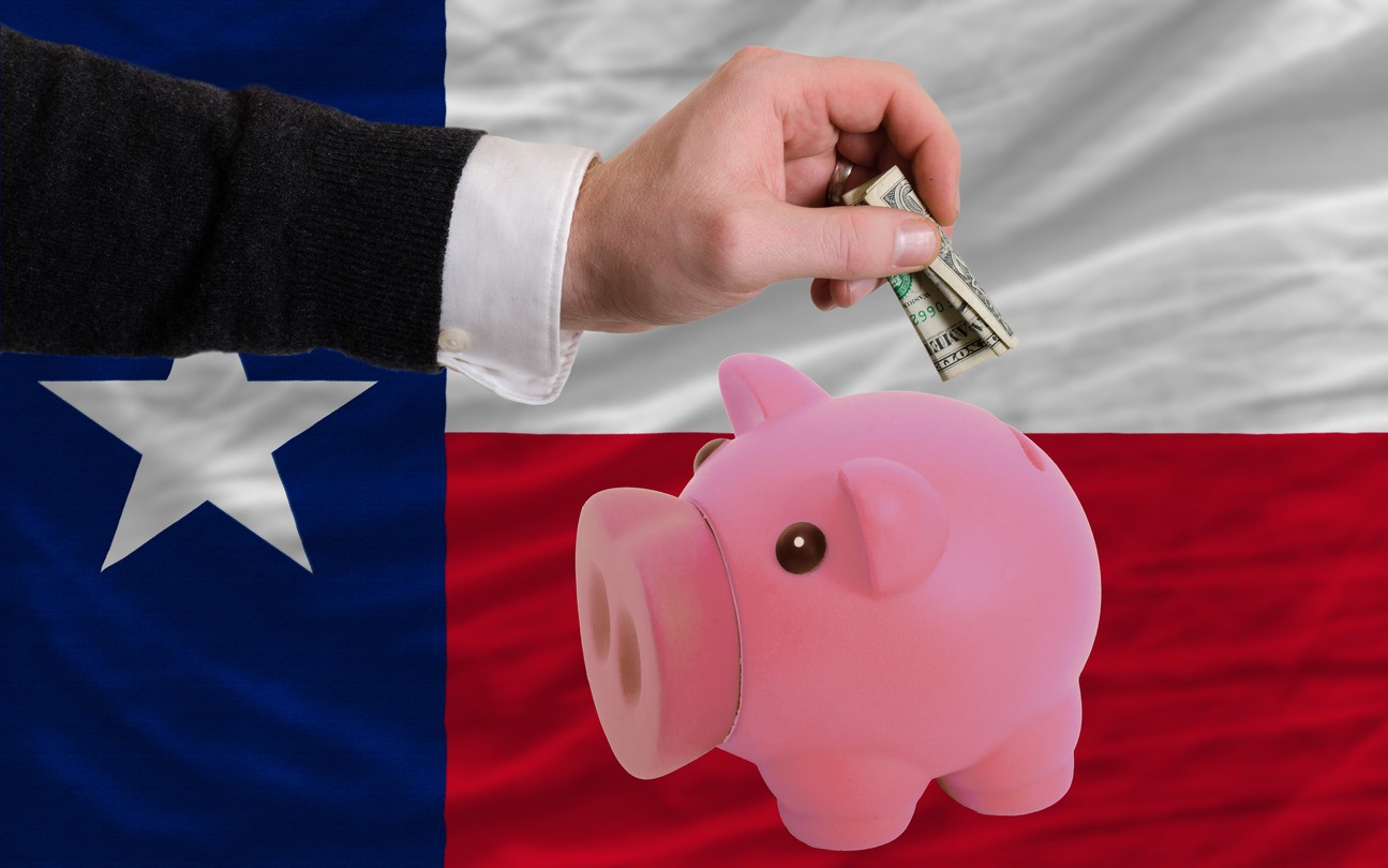 man putting dollar in a piggy bank with flag of Texas on the background