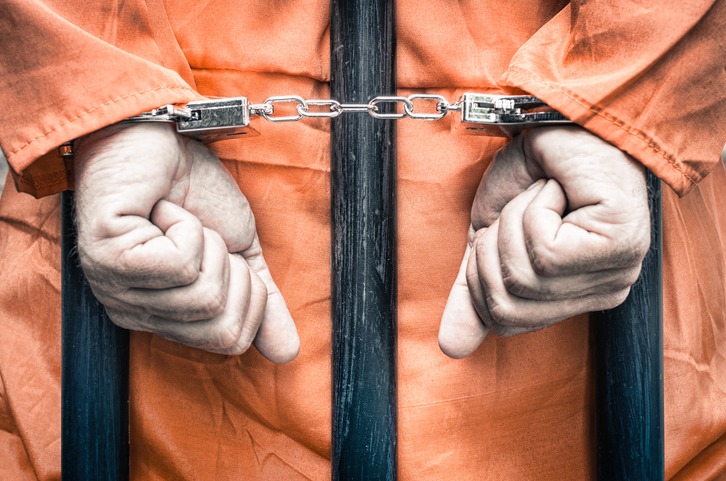 Handcuffed hands of a prisoner behind prison bars