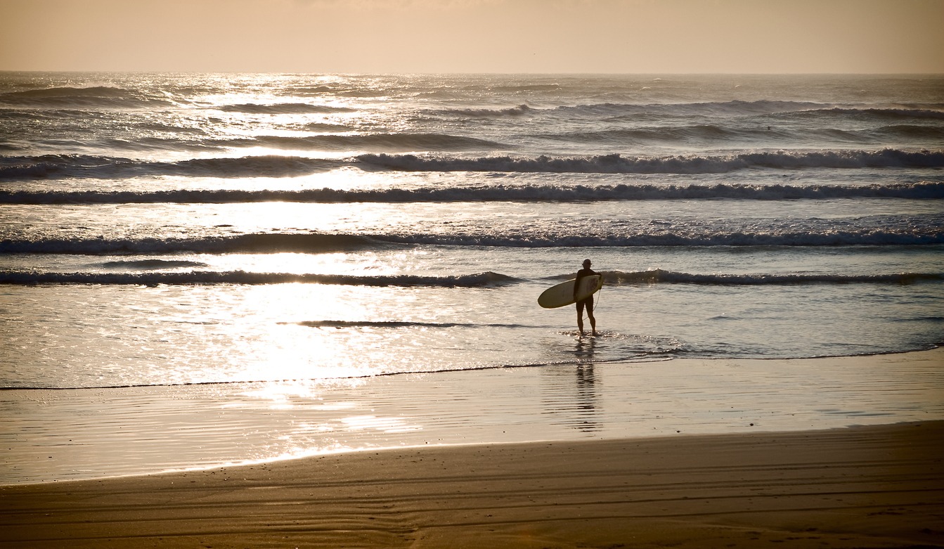 a man at sunrise looking out at the ocean with his surfboard
