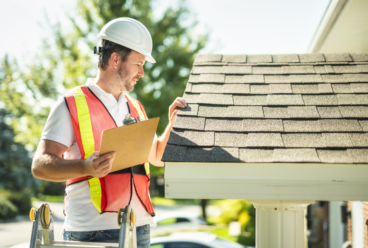 a man with hard hat standing on steps inspecting house roof